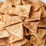 A bowl of cinnamon chips surrounded by baking ingredients on a rustic wooden table.