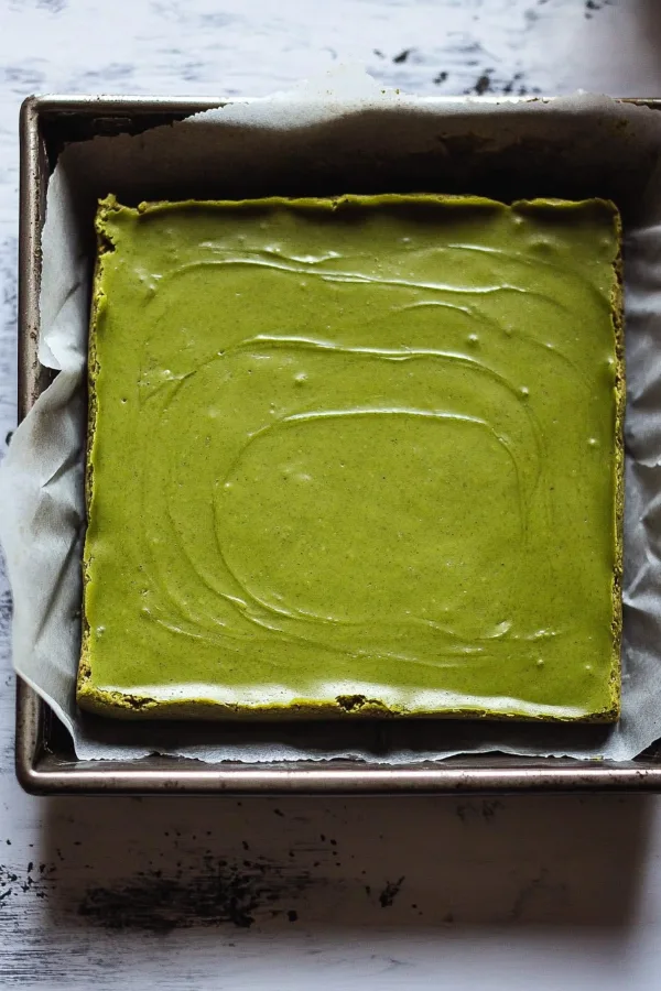 Mixing matcha brownie batter in a glass bowl with a whisk, capturing the vibrant green color.