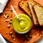 Creamy homemade pistachio butter in a jar with pistachios and toast