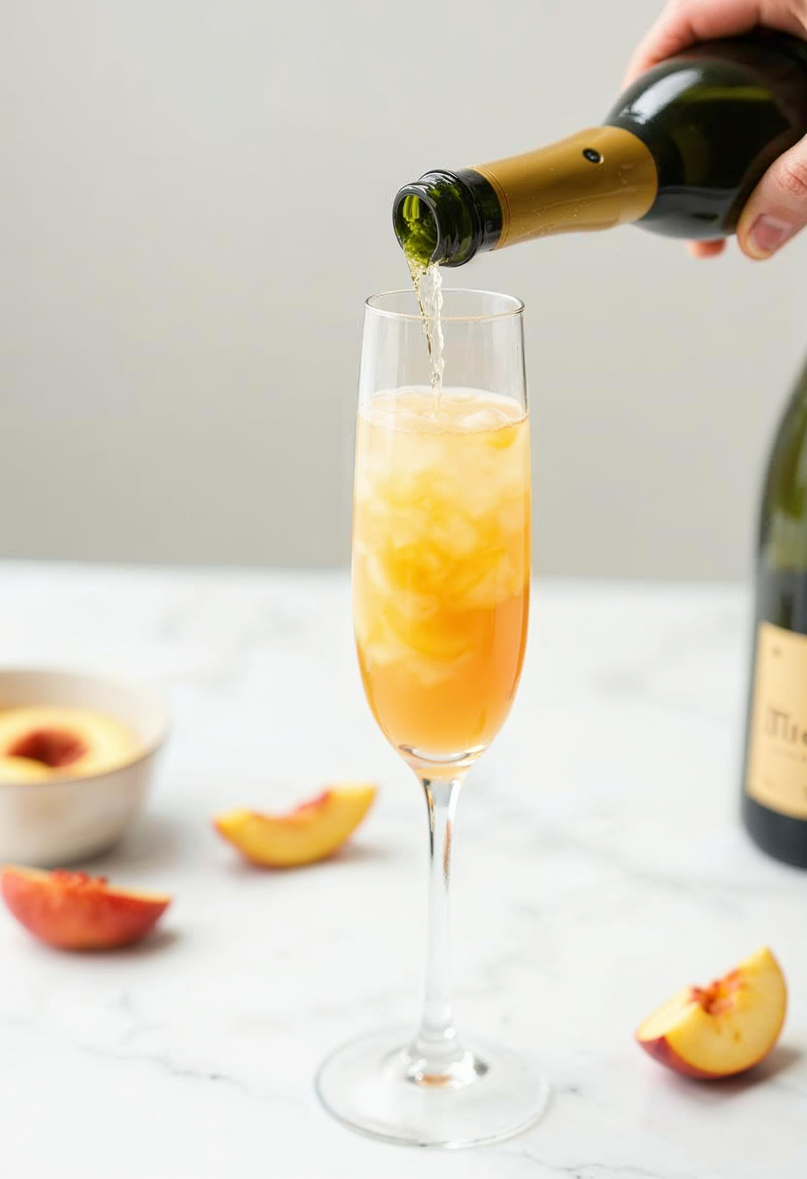 Pouring Prosecco into a glass with peach puree to make a Bellini.